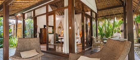 An open-air lounge with wicker furniture, a wooden floor, and a thatched roof.