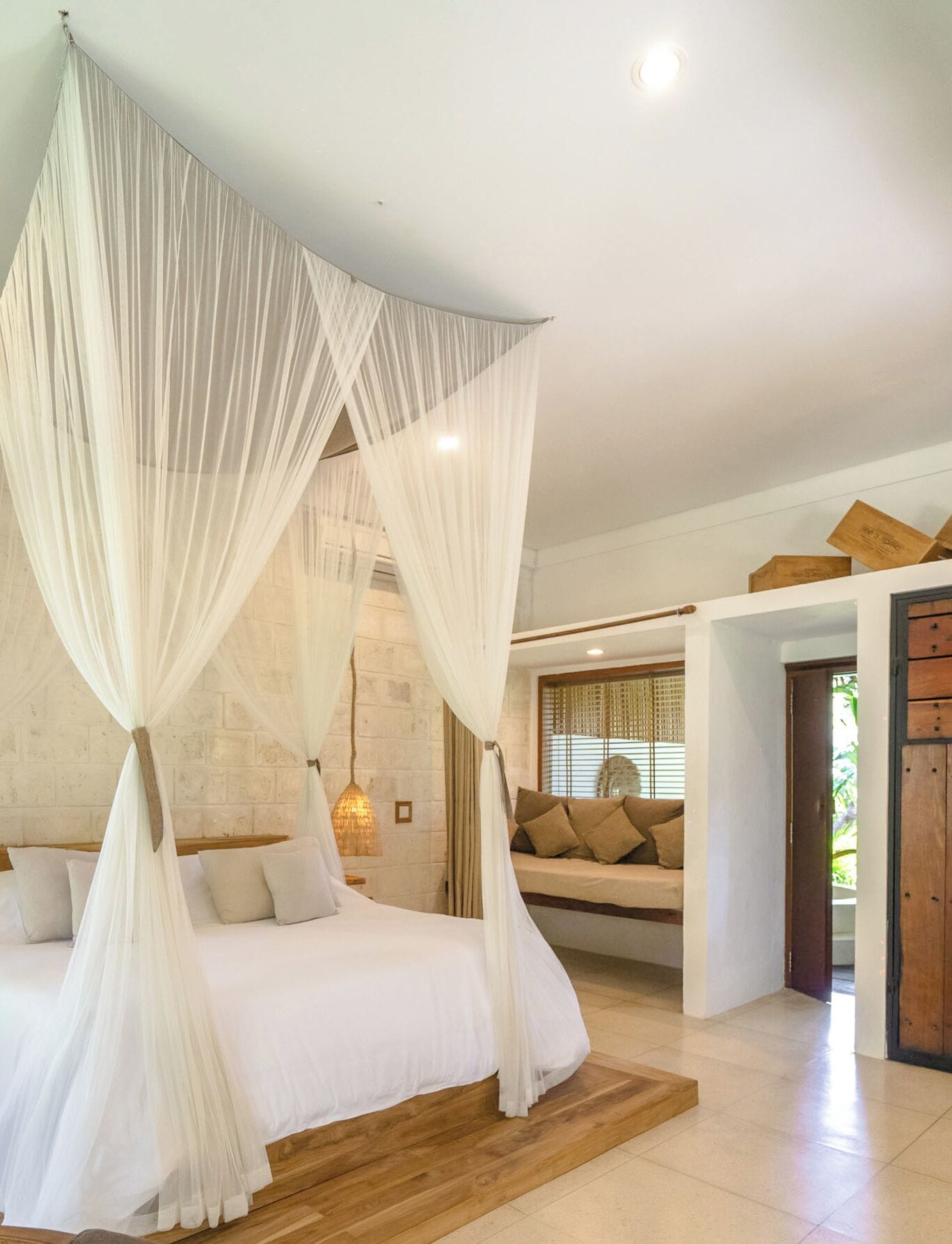 Une chambre à coucher avec un lit sous un dais, un canapé avec des coussins, un plancher en bois et une vue sur l’extérieur.