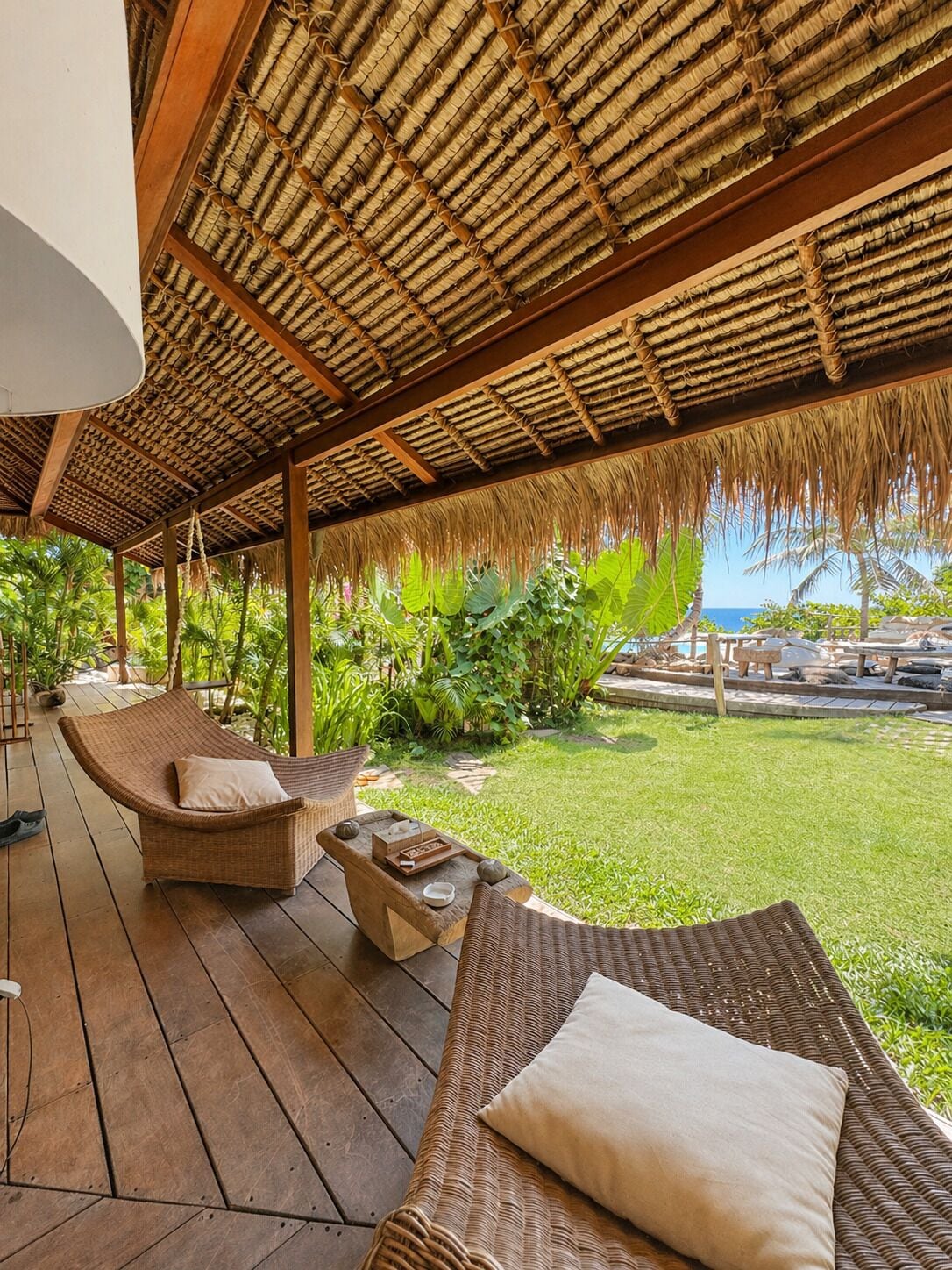 A covered outdoor area with wicker furniture, a thatched roof, and a view of the ocean.