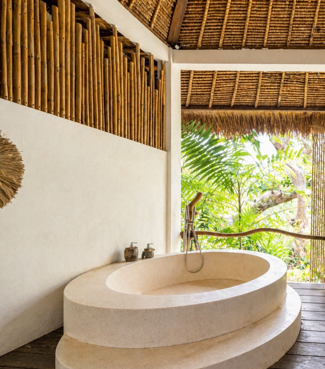 A circular stone bathtub in a room with a thatched roof and bamboo wall paneling.