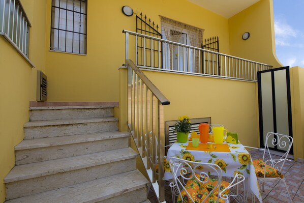 A yellow building with a staircase and a table set with a sunflower tablecloth.