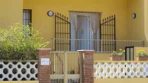 A yellow building with a gated entrance, a balcony with a metal railing, and potted plants on the balcony. - Fiori Gialli Caucana (Santa Croce Camerina)