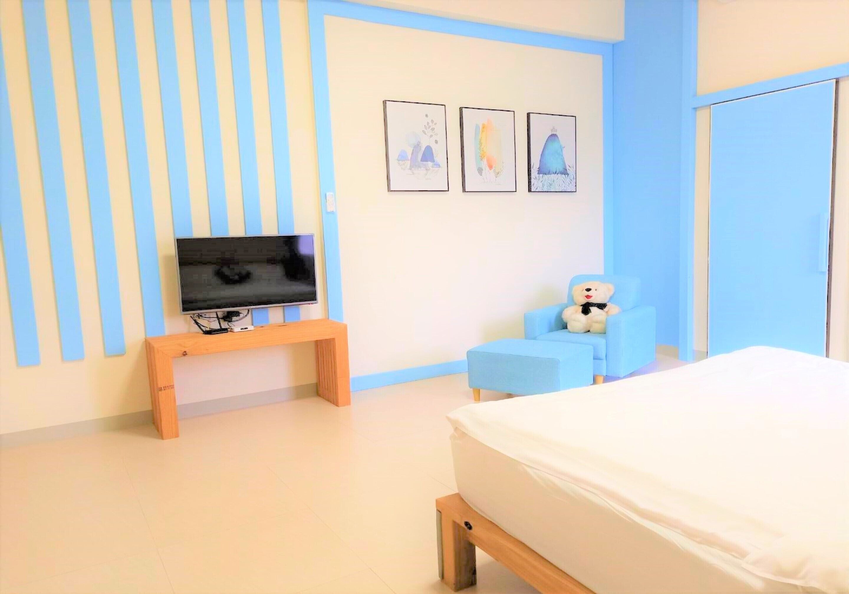 A bedroom with a bed, a TV on a stand, a chair, and three wall art pieces.