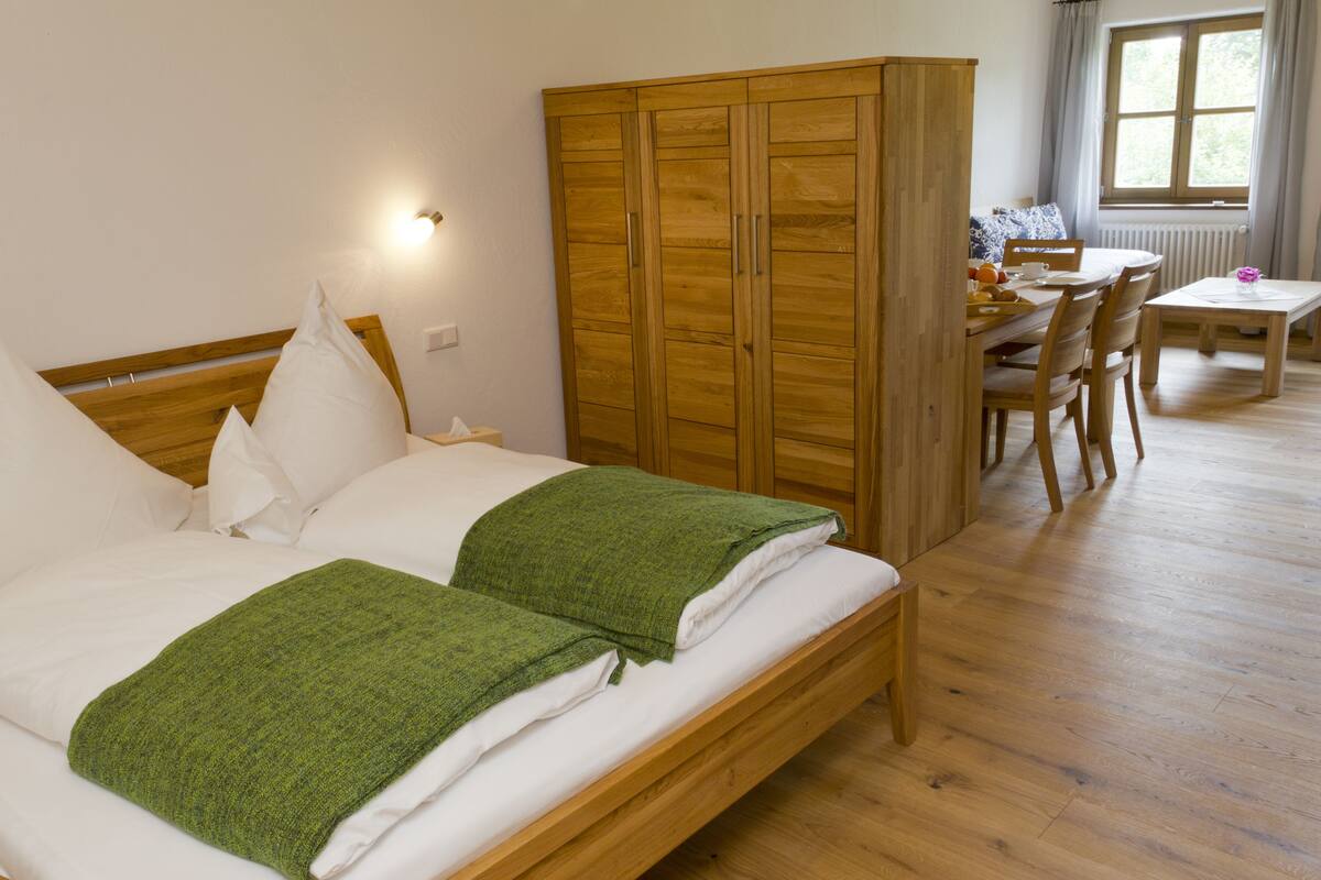 A bedroom with two beds, a wooden wardrobe, a dining table with chairs, and a window with curtains.