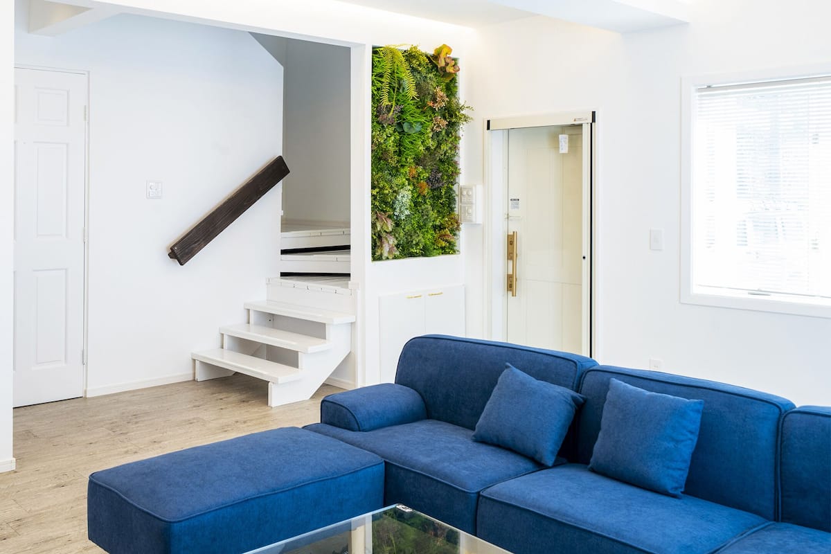 A modern living room with a blue sofa, a glass coffee table, and a staircase with a white railing.