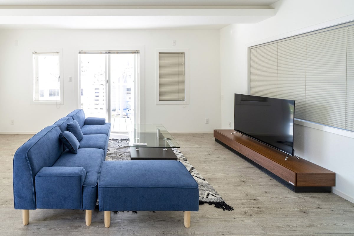 A modern living room with a sectional sofa, a glass coffee table, and a flat-screen TV on a wooden stand.