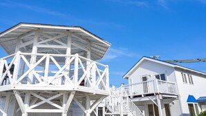 A white wooden observation tower with a balcony, attached to a white house with a blue roof and a balcony. - Villa Kanutan (Motobu)