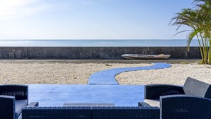 A beachside seating area with a concrete barrier, a boat, and a palm tree. - Villa Kanutan (Motobu)