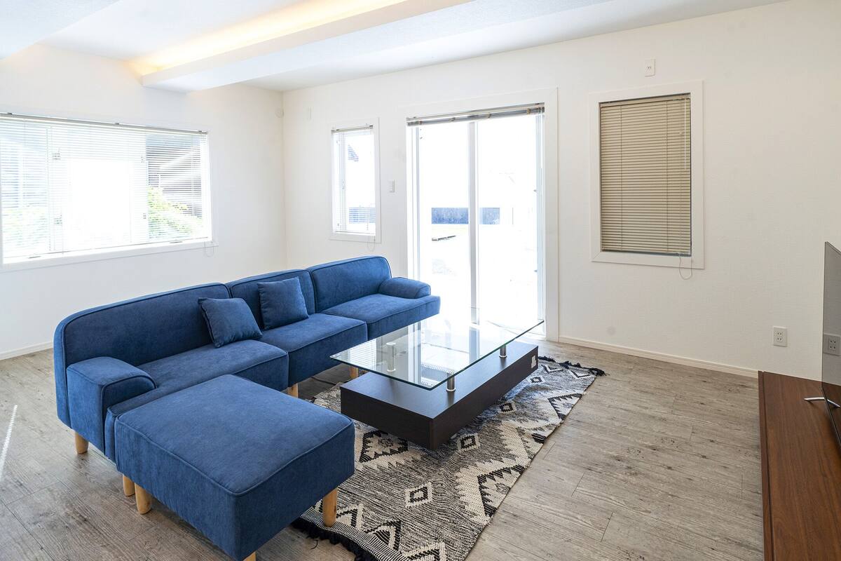 A living room with a blue sectional sofa, a glass coffee table, and a flat-screen TV.