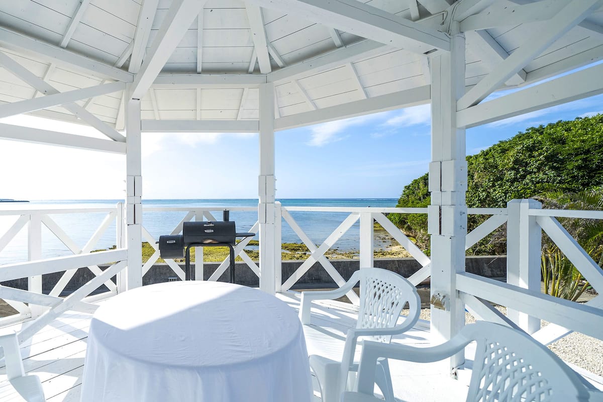 A covered outdoor area with a table and chairs, overlooking a body of water and greenery.
