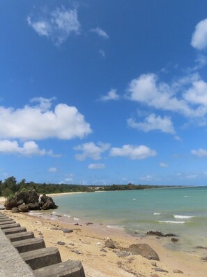 A beach with clear blue sky, calm sea, and a concrete staircase leading down to the shore. - Villa Kanutan (Motobu)