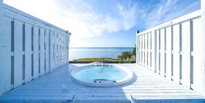 Um deck de madeira com uma banheira de hidromassagem e vista para o oceano.