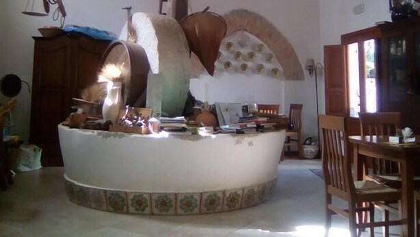 A room with a high arched ceiling, a central round table with various items, and hanging baskets. - Agriturismo Castelluzzo (Custonaci)