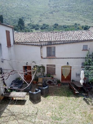 A rustic courtyard with a tiled-roof building, outdoor seating, and a hanging clothesline. - Agriturismo Castelluzzo (Custonaci)