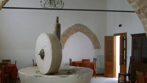 A circular stone structure with a central pillar, surrounded by chairs and tables, in a room with an arched doorway and a chandelier. - Agriturismo Castelluzzo (Custonaci)