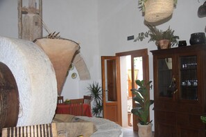 A room with a large stone sculpture, a wooden cabinet with glass doors, and a door leading to an outdoor area. - Agriturismo Castelluzzo (Custonaci)
