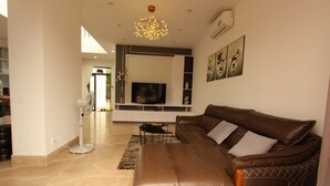 A modern living room with a brown leather sofa, a TV mounted on a white wall, and a decorative ceiling light. - Seaview Winner Pool Villa (Ho Chi Minh City)