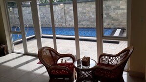 A room with large windows overlooking a swimming pool, wicker furniture, and a stone wall. - Seaview Winner Pool Villa (Ho Chi Minh City)