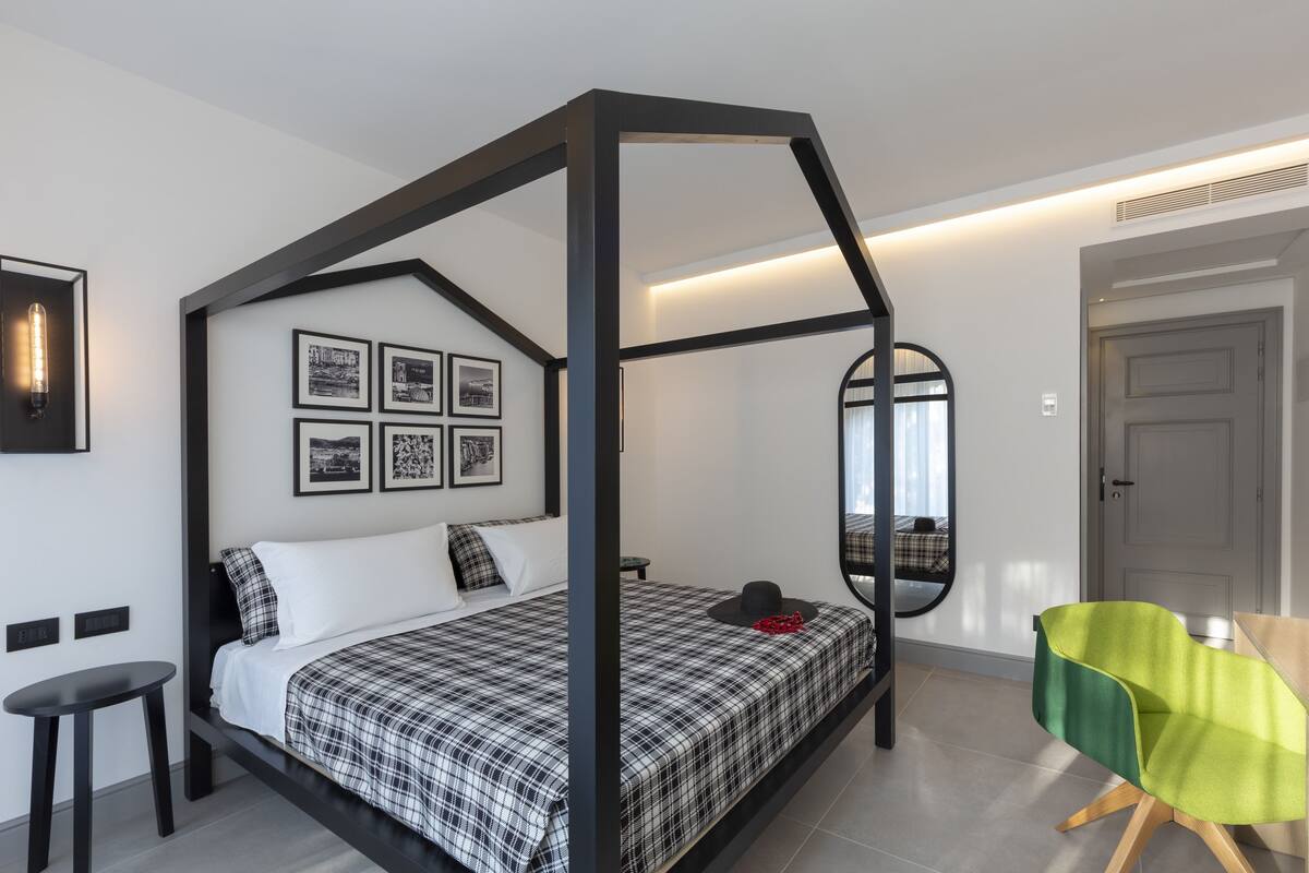 A modern bedroom with a four-poster bed, a small table, a chair, and a mirror on the wall.