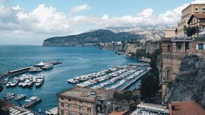 A coastal marina with numerous boats docked, a rocky cliffside, and buildings with balconies overlooking the water. - Maison Bon Bon (Sorrento)