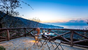 A stone patio with a table and chairs overlooking a scenic view of a body of water and hills. - Maison Bon Bon (Sorrento)