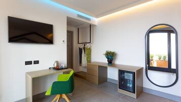 A modern hotel room with a desk, a green chair, a minibar, a television, and a large mirror.