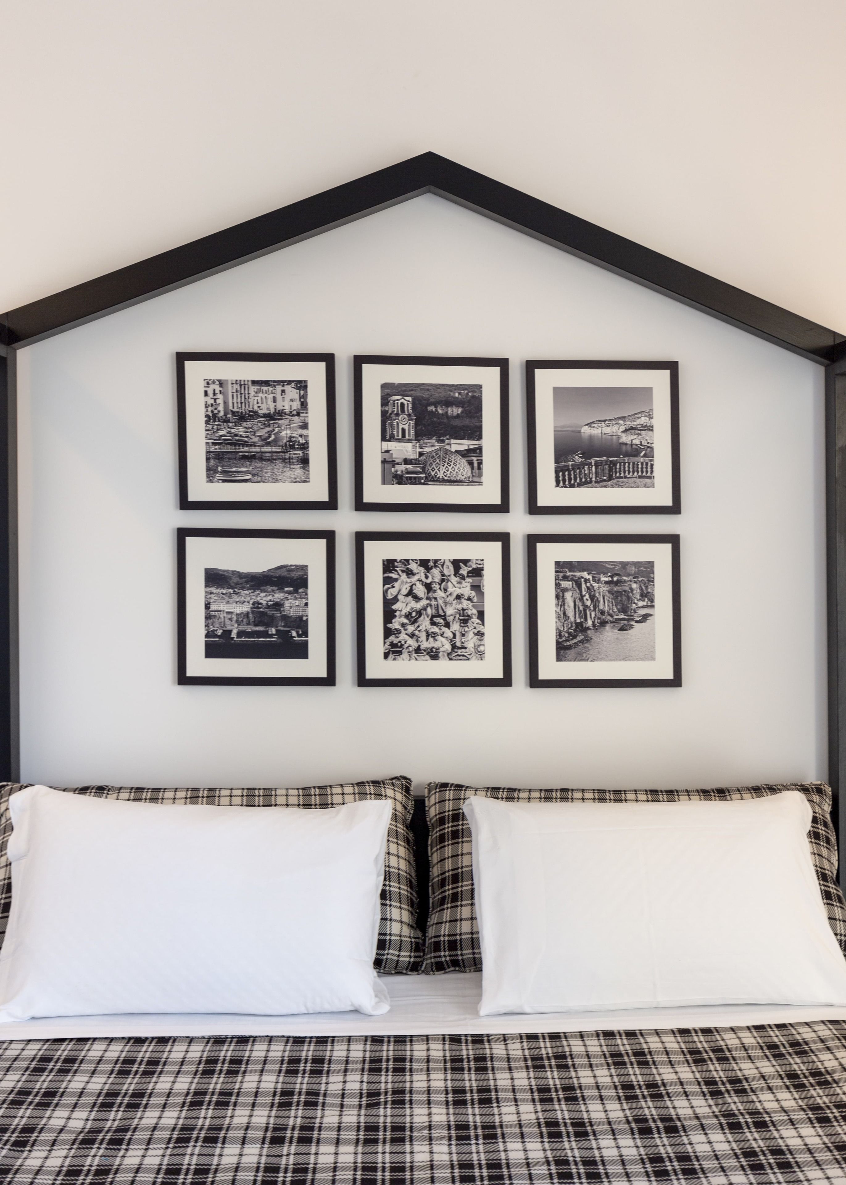 A bedroom with a bed featuring plaid bedding, a headboard with a black frame, and six black-and-white photographs on the wall.