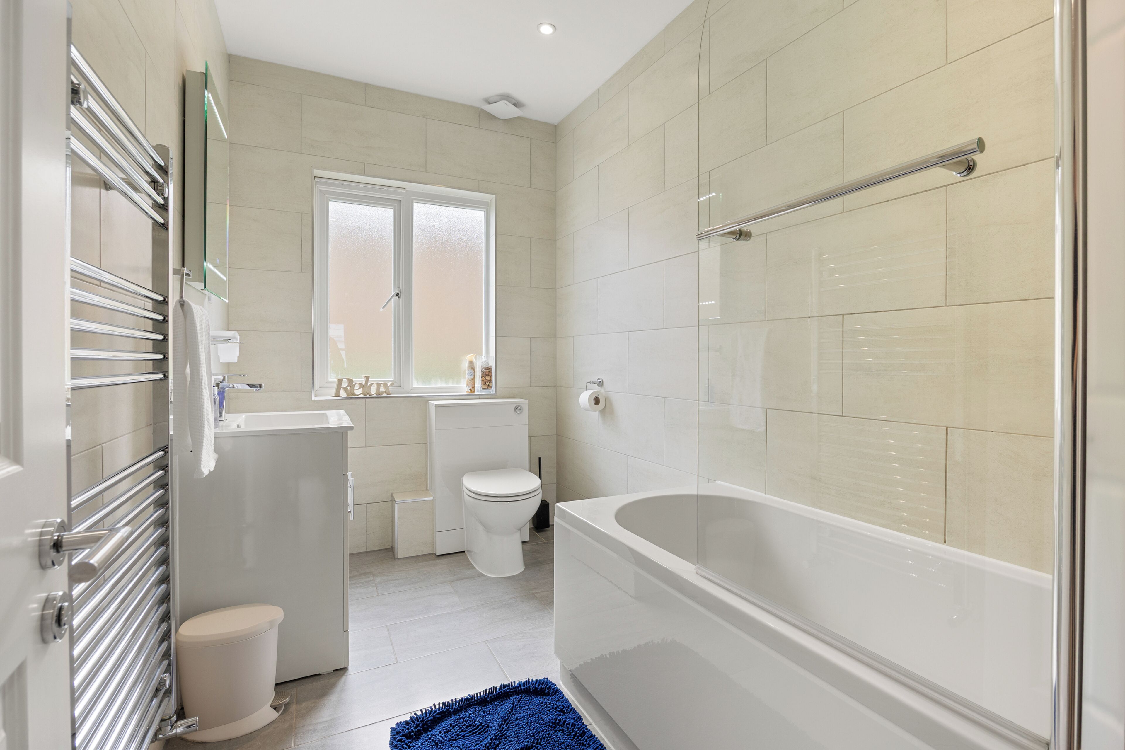 A modern bathroom with a bathtub, toilet, and a window.