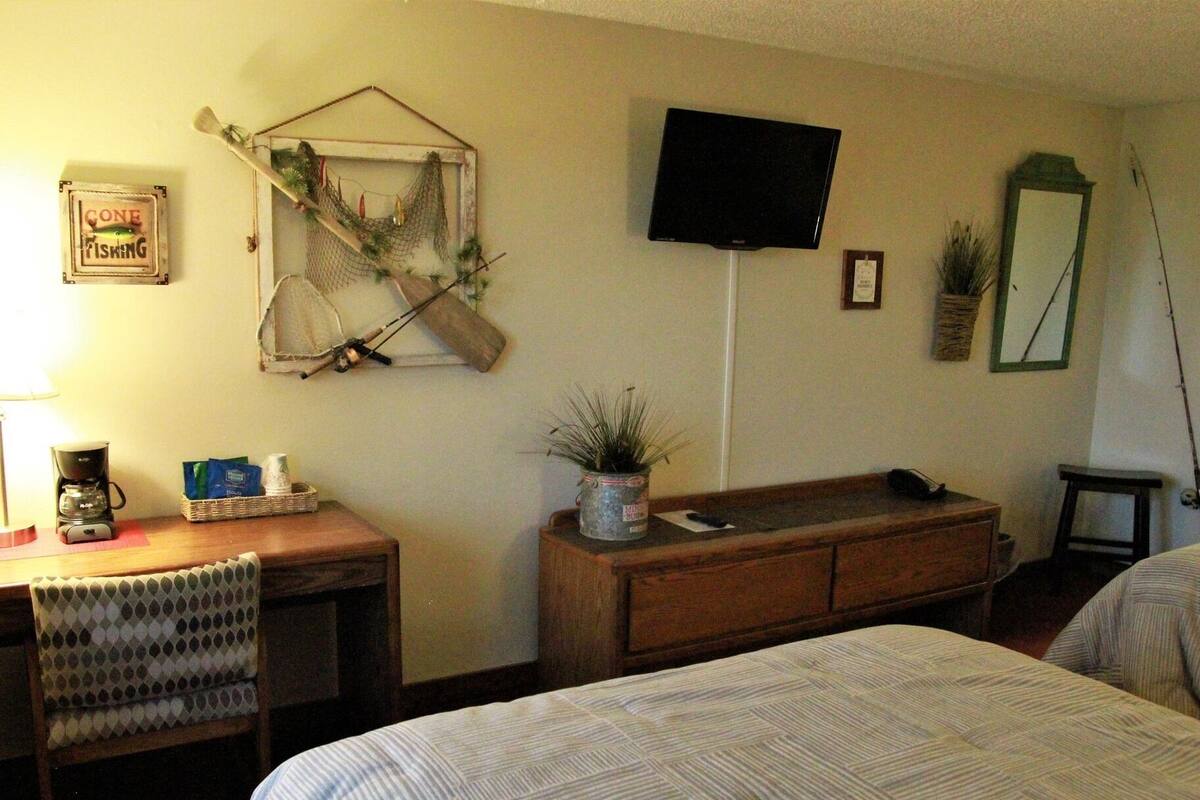 Habitación de hotel con cama, escritorio con cafetera, televisor, espejo y una decoración con red de pesca.