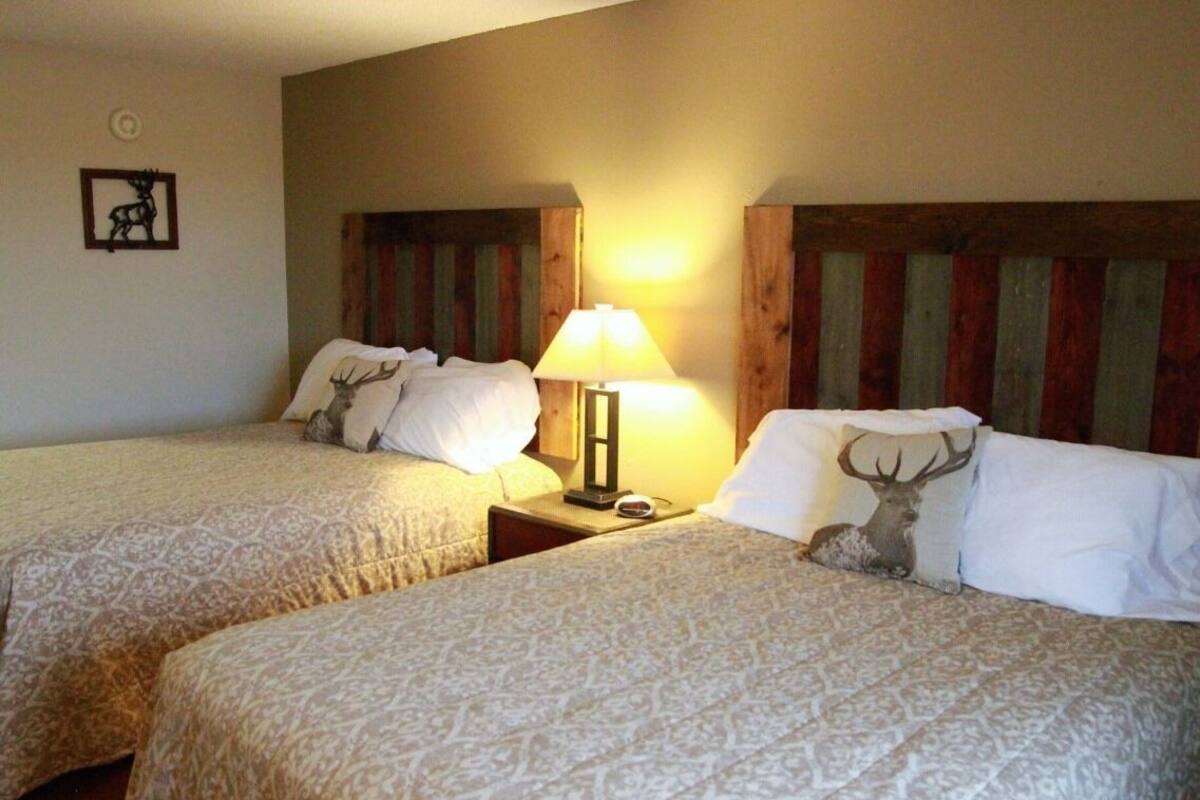 Dos camas individuales con ropa de cama estampada, una mesita de noche con lámpara y una almohada con motivos de ciervo.