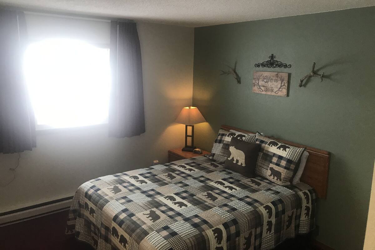 Un dormitorio con cama, mesita de noche, lámpara, ventana con cortinas y adornos en la pared.