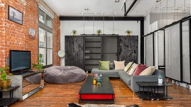 Ein modernes Wohnzimmer mit freiliegenden Backsteinwänden, einem Flachbildfernseher, einer Couch, einem Couchtisch und einem großen Fenster.