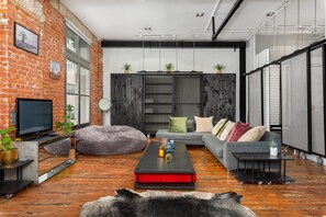 Un salon moderne avec des murs en briques apparentes, un téléviseur à écran plat, un canapé, une table basse et une grande fenêtre.