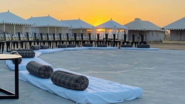 A row of tents with a flat rooftop area, some with tables and chairs, and a sunset in the background. - Aroma Desert Safari Camp (Jaisalmer)