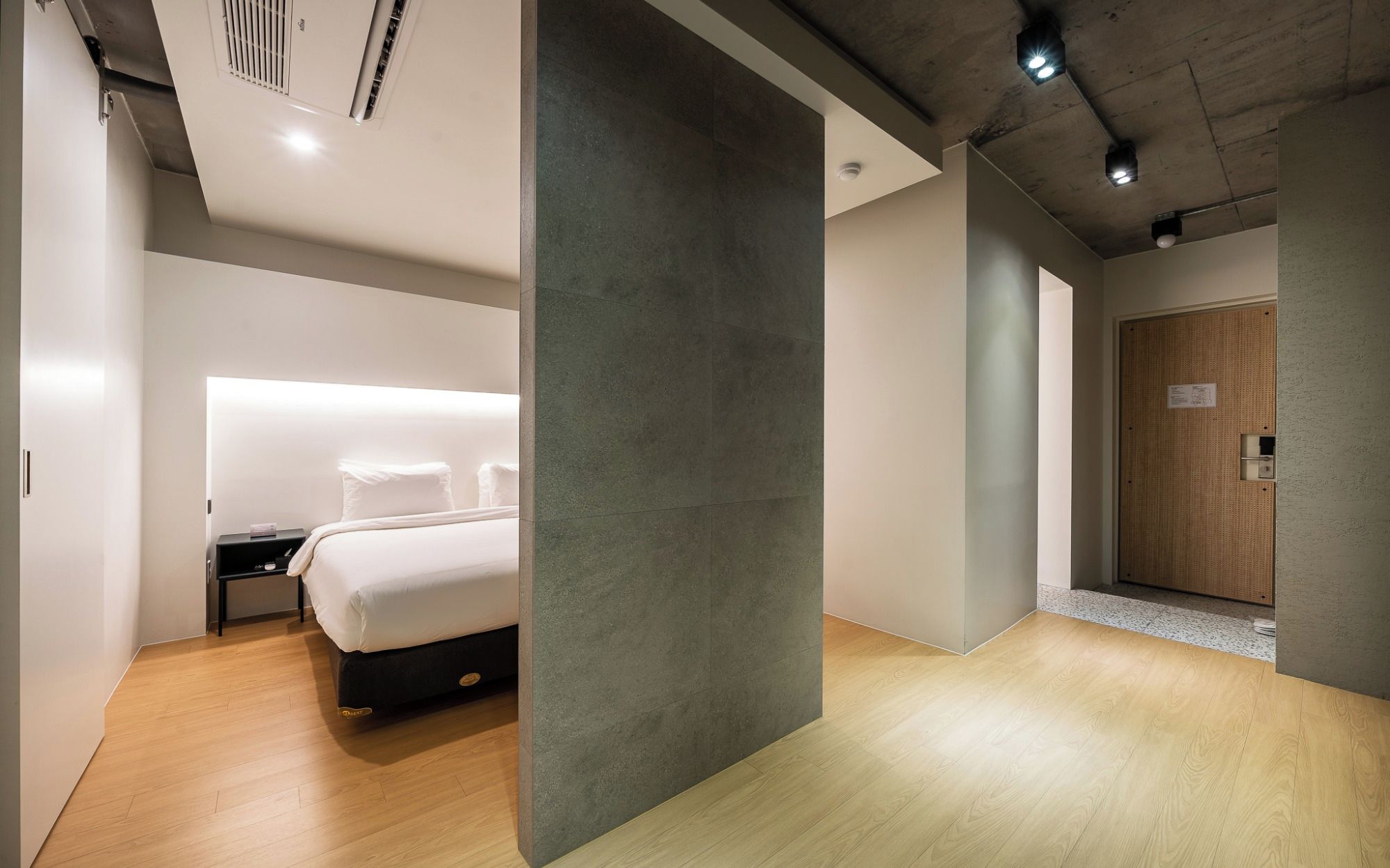 A modern hotel room with a bed, bedside table, and a wardrobe.