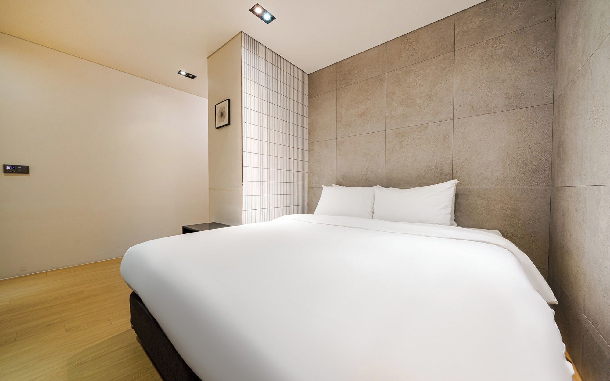 A modern hotel room with a large bed, a wall-mounted control panel, and a tiled accent wall.