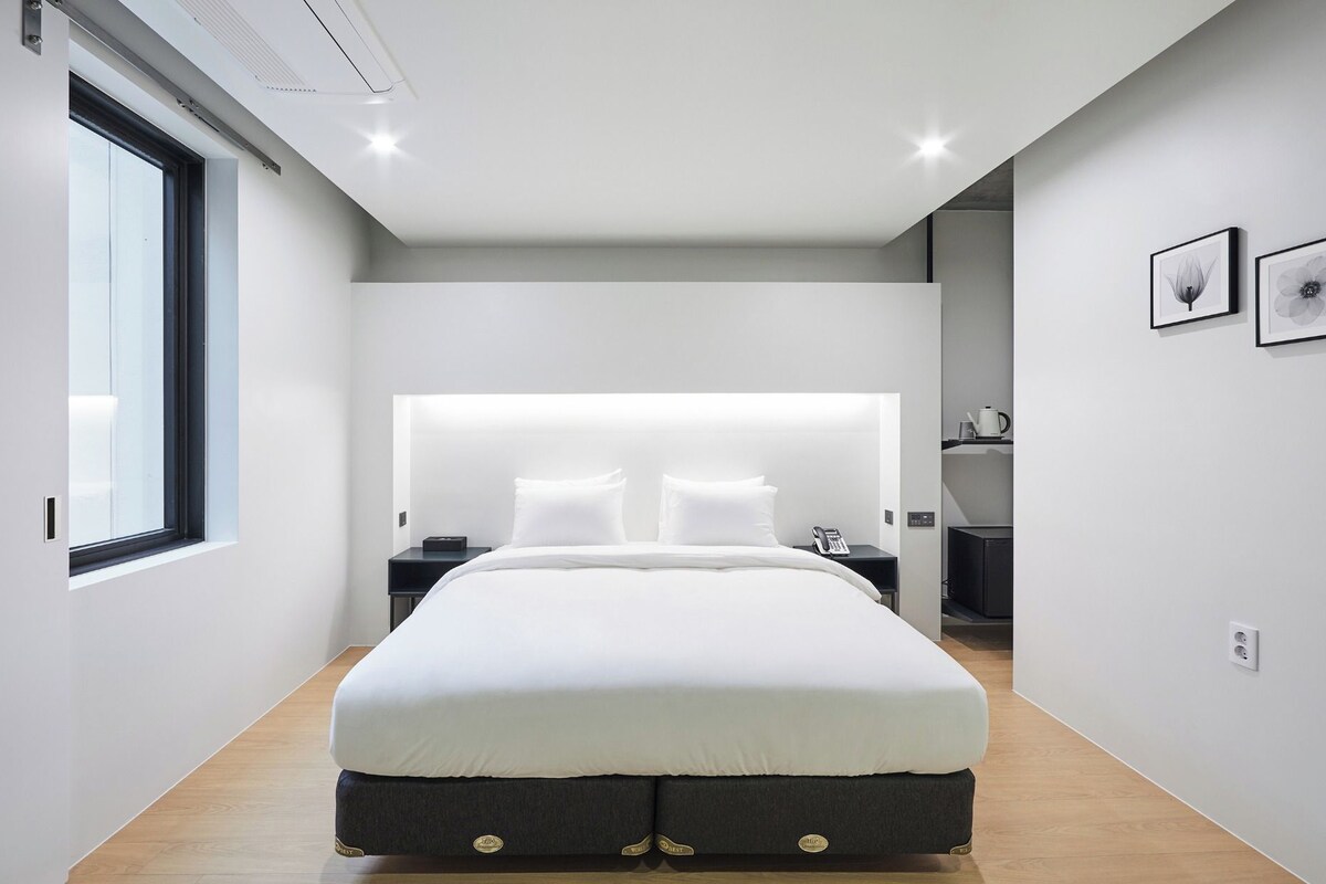 Un dormitorio moderno con una cama grande, mesitas de noche, una lámpara de noche, una ventana y cuadros en la pared.