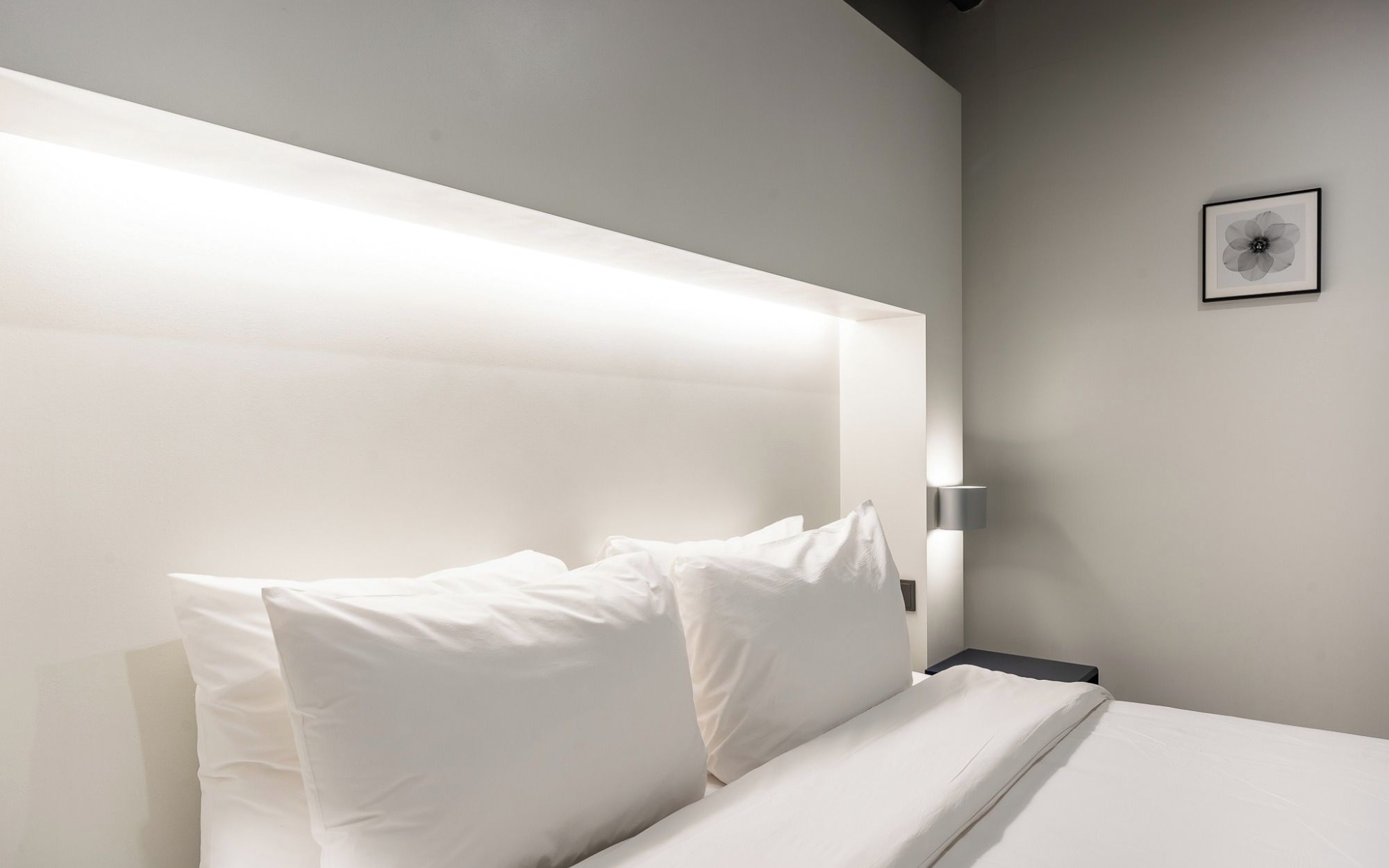 A modern bedroom with a large bed, white linens, and a wall-mounted light fixture.