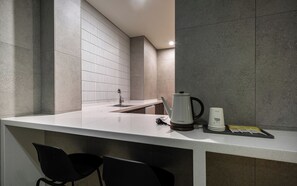 Een moderne keuken met een wit aanrecht, een waterkoker, een koffiezetapparaat en een set zwarte stoelen.