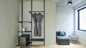 Una camera moderna dal design minimalista, con un divano grigio, un tavolino, un mobile contenitore nero e una rastrelliera a parete con vestiti.