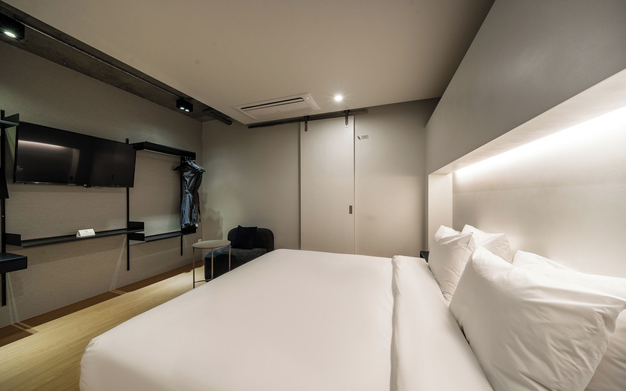 A modern hotel room with a large bed, a flat-screen TV mounted on the wall, a small table, and a wardrobe.