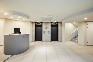 Un área de recepción moderna con un mostrador curvo, dos ascensores y una escalera.