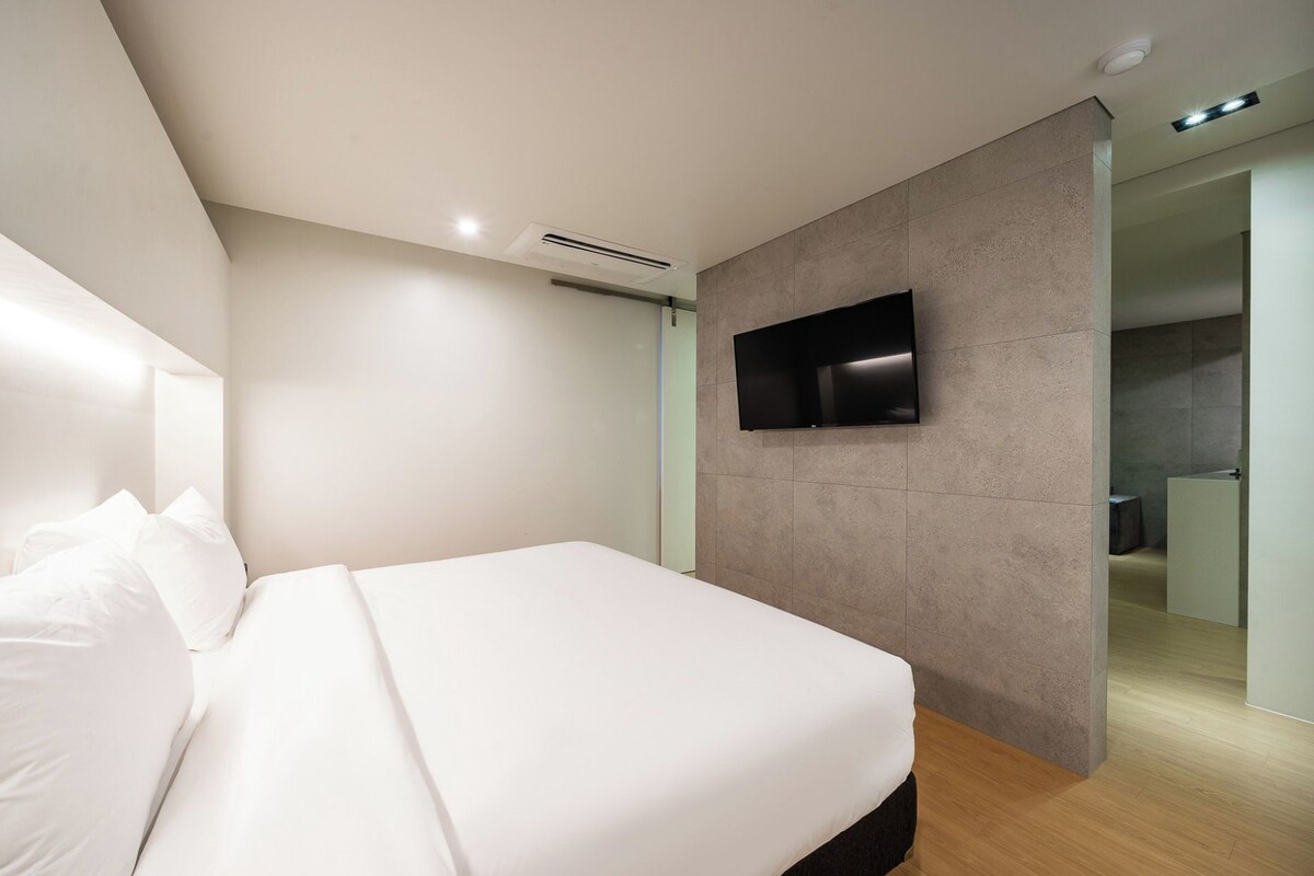 Un dormitorio moderno con una cama grande, un televisor montado y un baño a la vista.