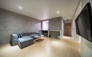 Een moderne woonkamer met een grijze modulaire bank, een kleine ronde tafel, en een keuken met een aanrecht en barkrukken.
