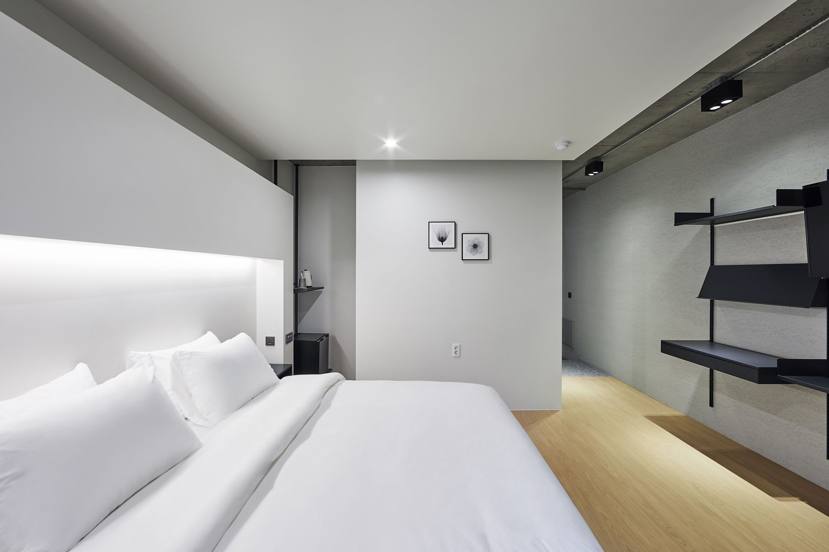 A modern hotel room with a large bed, a bedside table, and a built-in shelf unit.