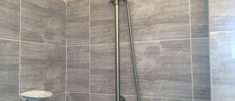 A shower with a handheld showerhead and a long hose, tiled walls, and a small shelf.