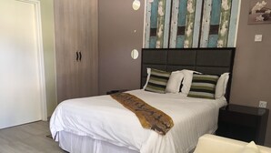 A bedroom with a bed, bedside tables, a chair, and a wardrobe. - Shumba Lodge (Tutume)