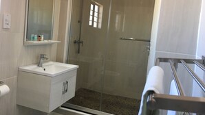 A modern bathroom with a glass-enclosed shower, a white sink with a mirror, and a towel rack. - Shumba Lodge (Tutume)