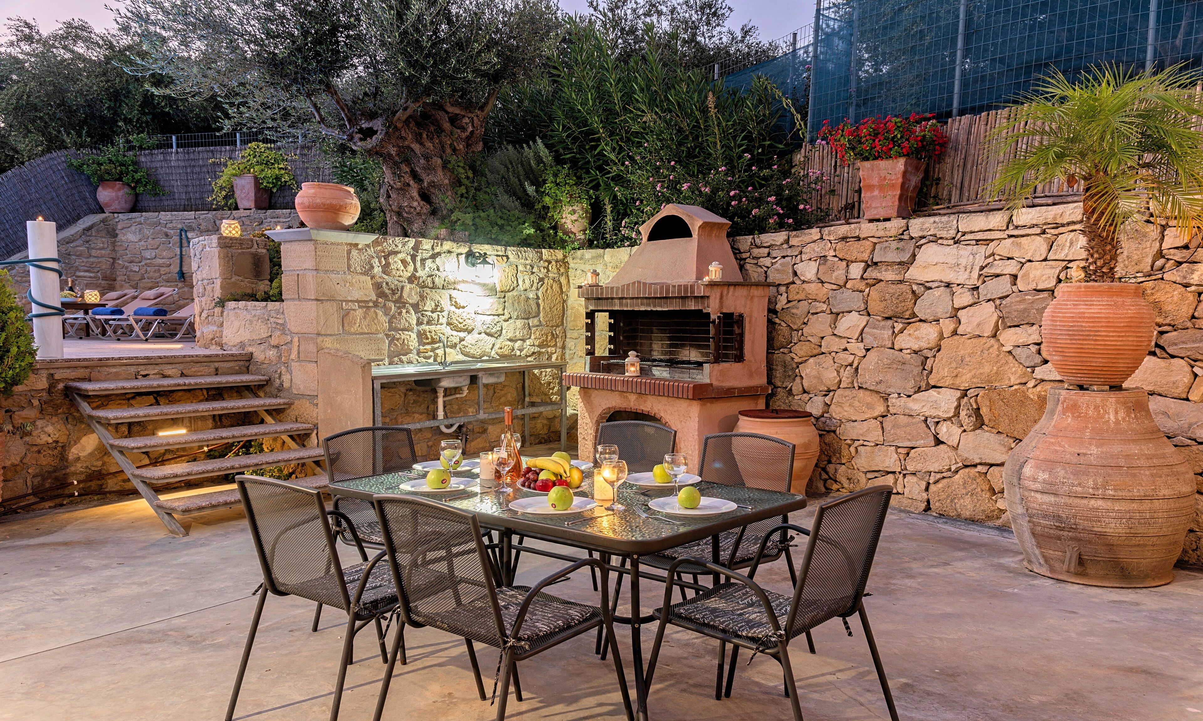 Un patio al aire libre con un muro de piedra, un horno de ladrillo y una mesa dispuesta para comer.