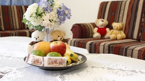 A dining table with a fruit plate, a vase of flowers, and two teddy bears on a striped sofa. - Na Na Ya Ji Bed and Breakfast (Taitung)